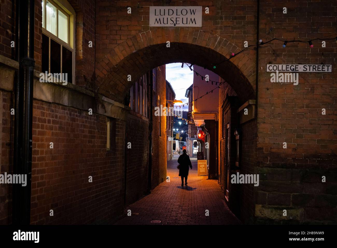 Una persona che cammina di notte attraverso un arco di mattoni su Church Street, uno stretto vicolo che corre attraverso College Street e Castle Square. Ludlow, Inghilterra Foto Stock
