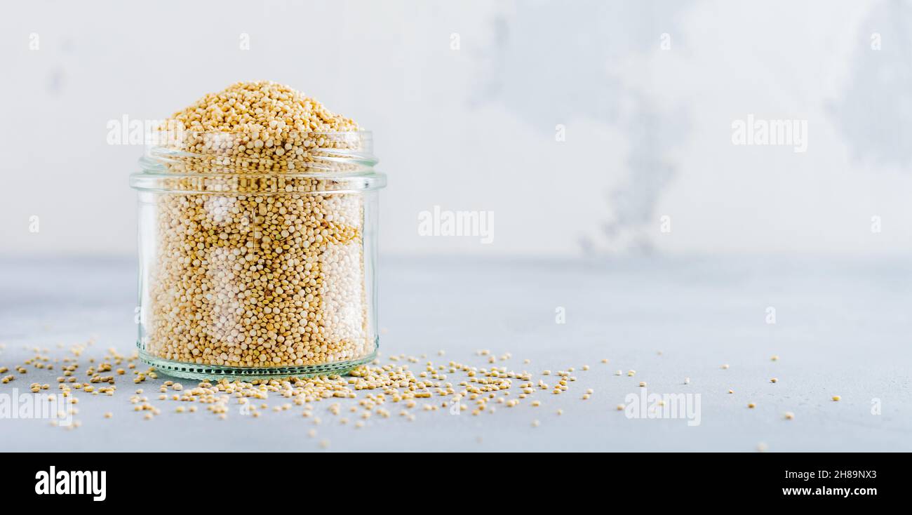 Grani di quinoa crudi in vaso. Cibo vegetariano sano su tavolo da cucina grigio. Messa a fuoco selettiva. Foto Stock