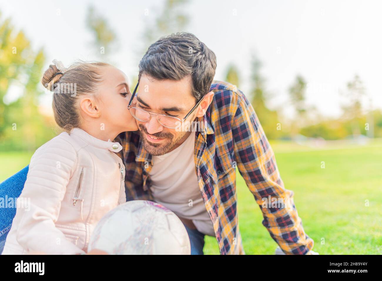 carina bambina baciando il suo padre in un parco Foto Stock