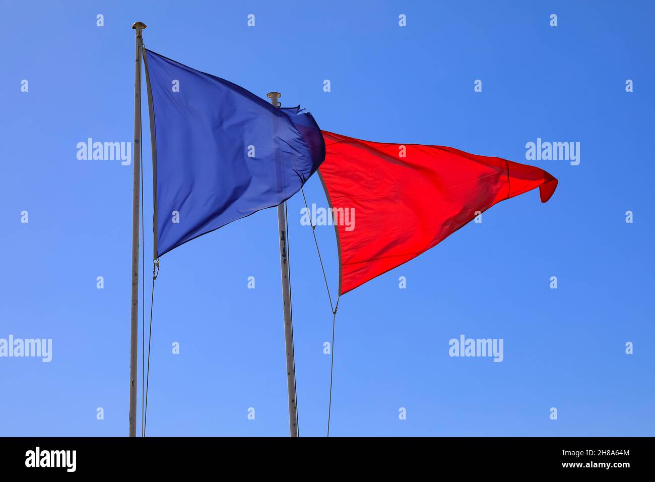 Due bandiere triangolari poste l'una accanto all'altra sui montanti soffiano nel vento per scopi di avvertimento e di informazione. Foto Stock