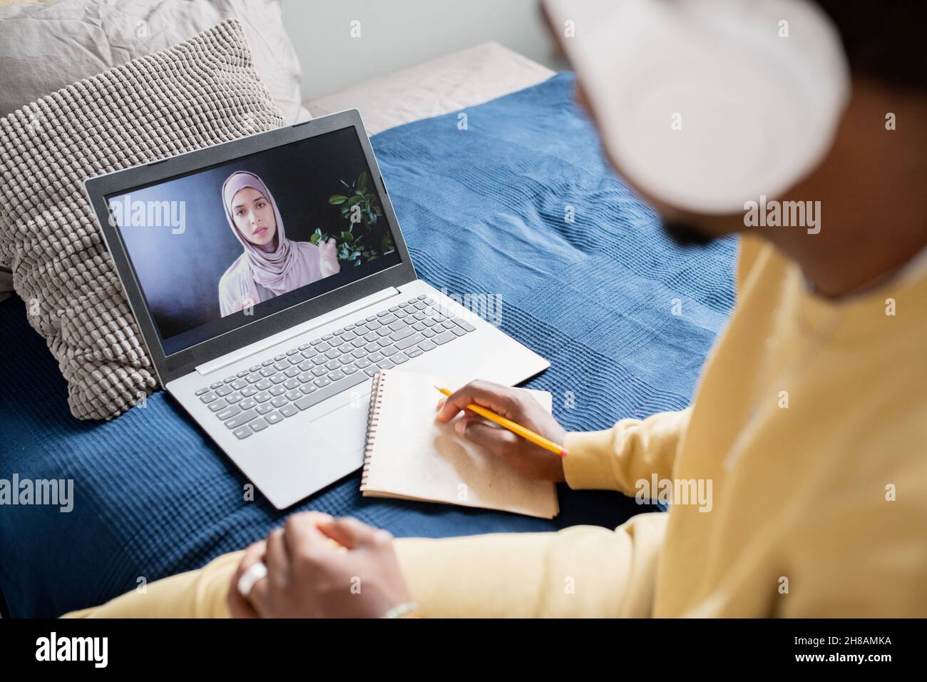 Giovane insegnante fiducioso in hijab spiegando punto di lezione allo studente con matita e blocco note durante la lezione online Foto Stock