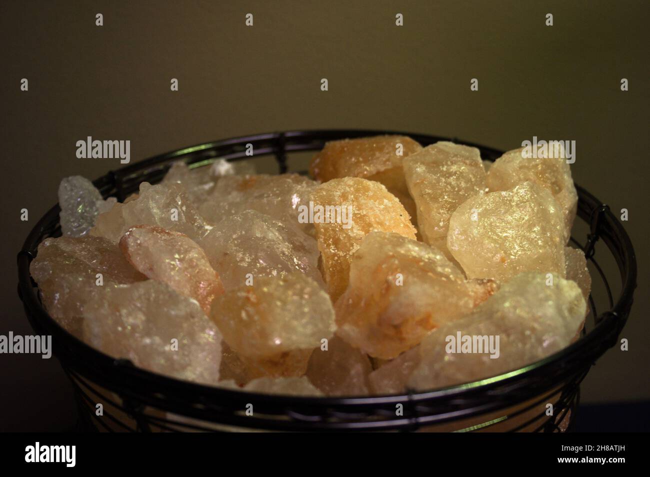 Cristalli di sale di Himalaya di pesca bianca e pallida in una ciotola di filo emettono un flusso morbido e calmante in una stanza fioca. Foto Stock