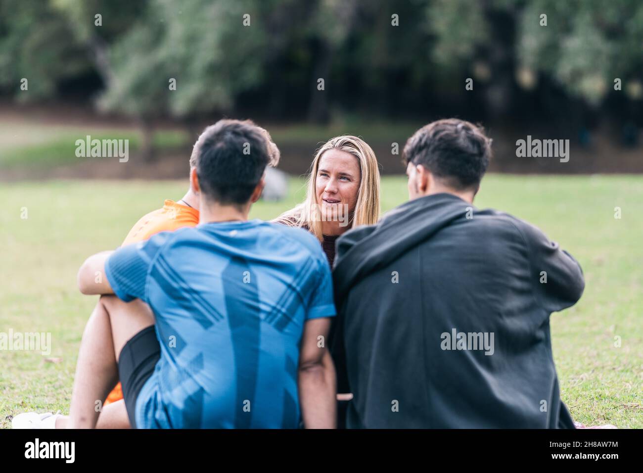 Gli amici chiacchierano mentre si siedono in un parco dopo una sessione di yoga Foto Stock