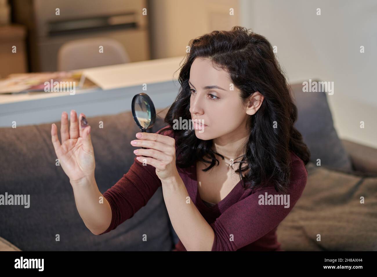 Messa a fuoco attraente femmina esaminando un cristallo attraverso una lente di ingrandimento Foto Stock