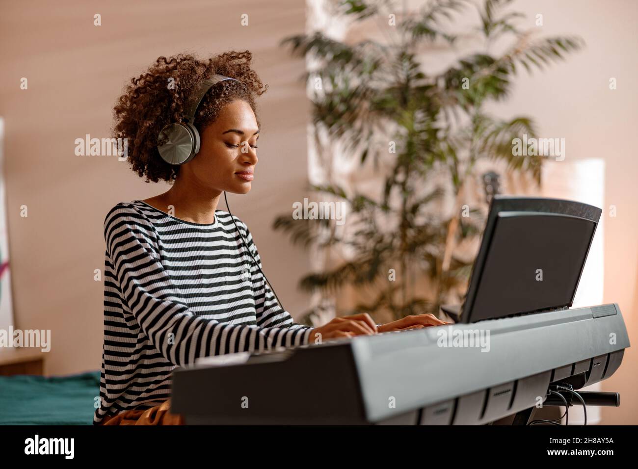 Donna afroamericana in cuffie che suona sintetizzatore a casa Foto Stock