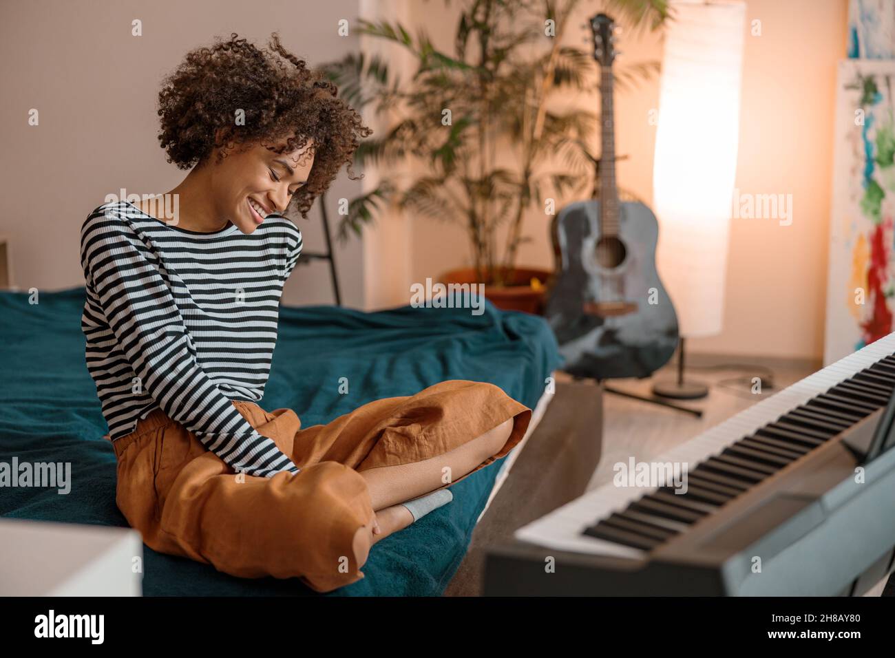 Gioiosa donna africana seduta vicino sintetizzatore a casa Foto Stock