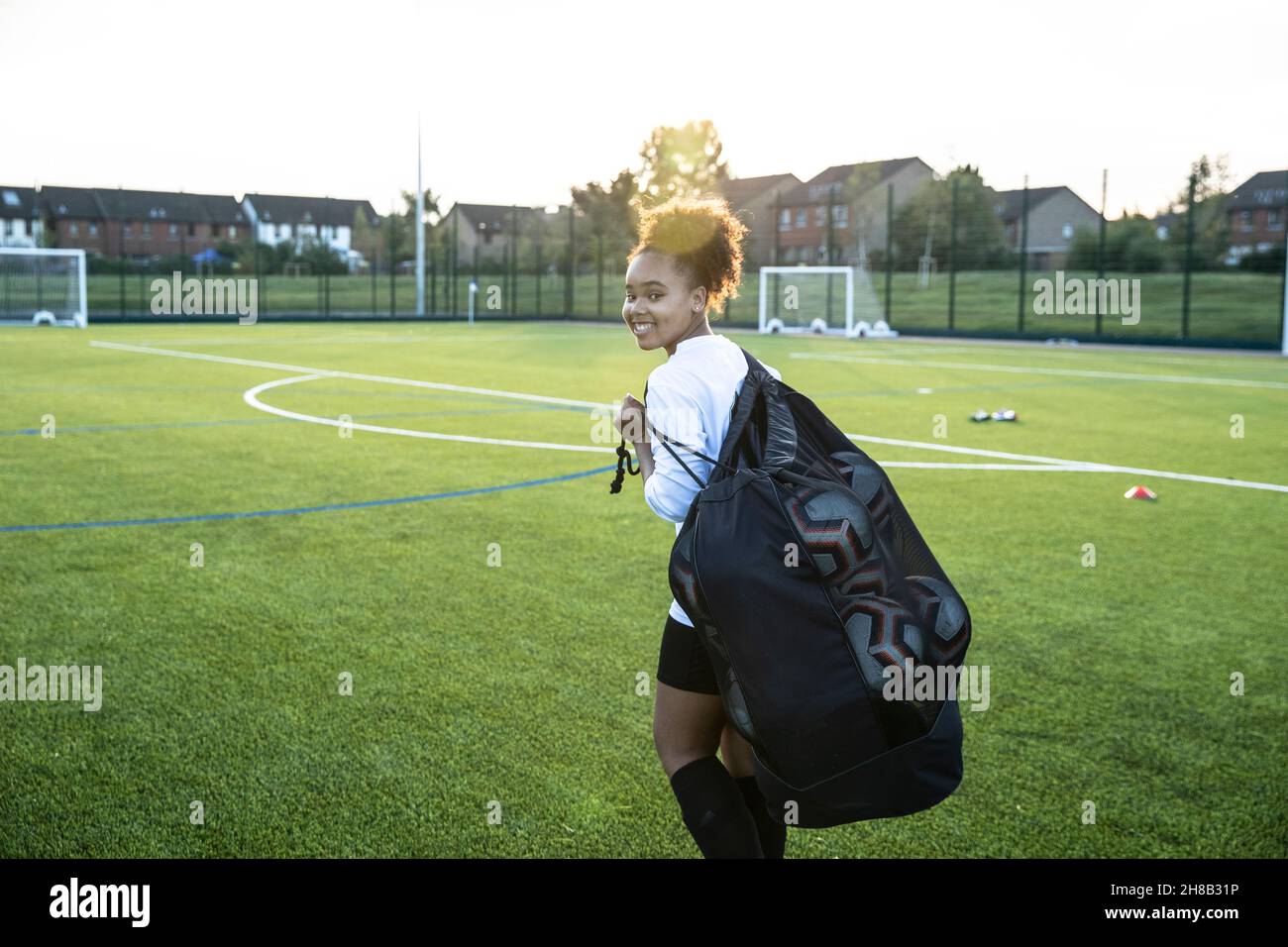 Regno Unito, giocatore di calcio femminile sorridente che trasporta la borsa con le sfere in campo Foto Stock