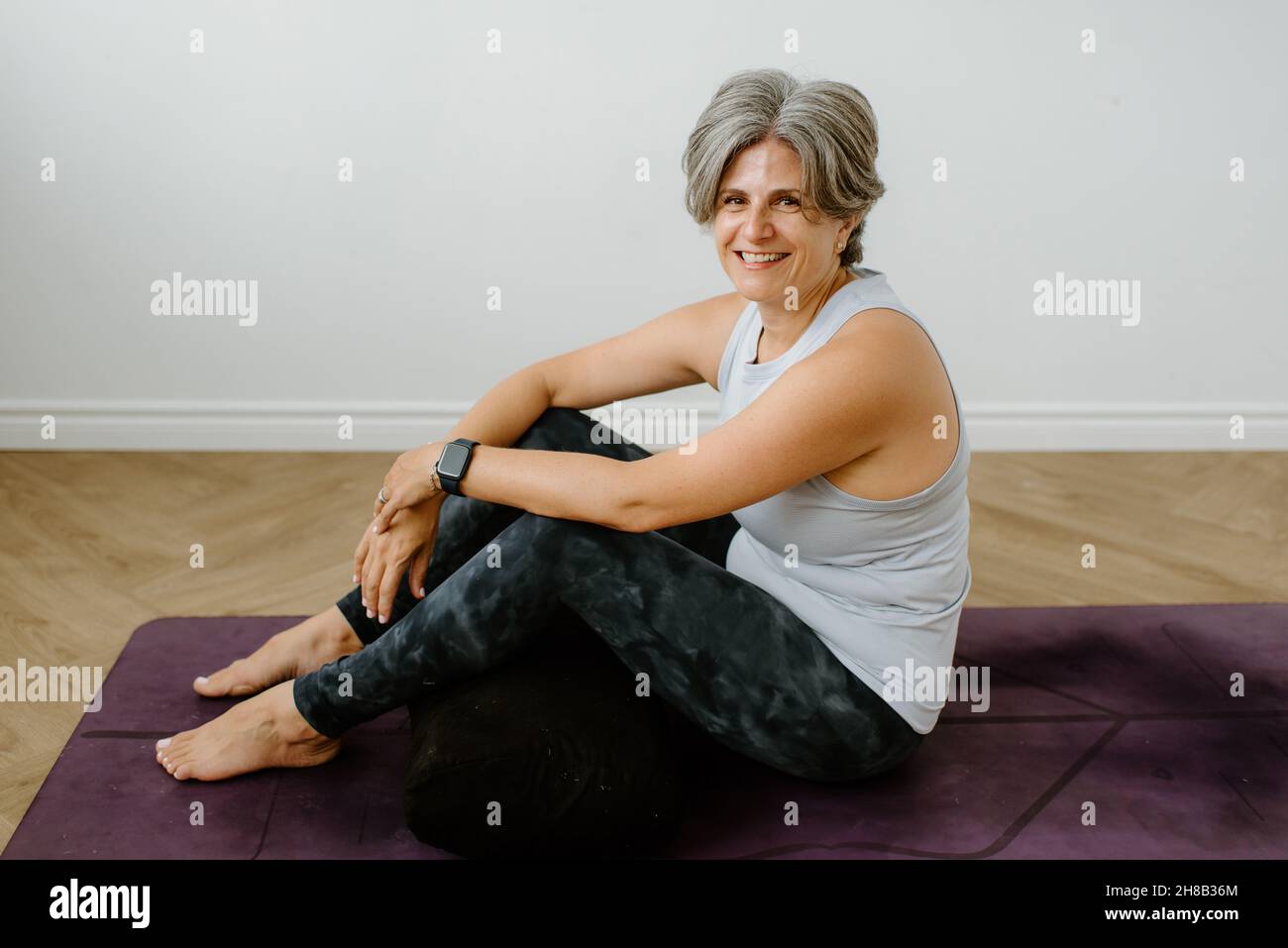 Ritratto di donna sorridente seduto sul tappeto di esercizio Foto Stock