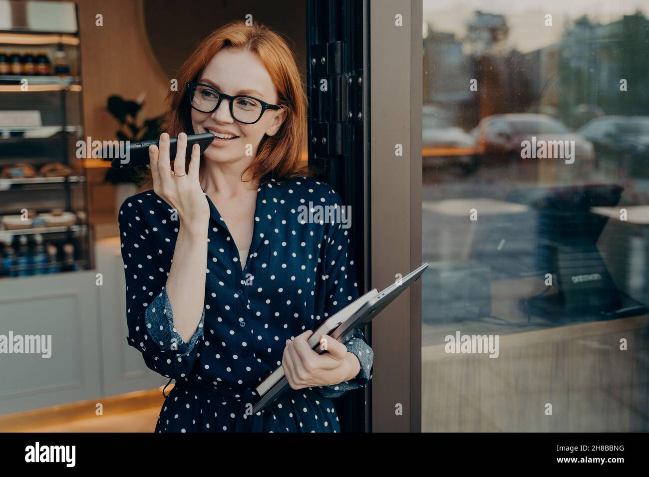 La freelance femminile è in piedi all'aperto con il telefono cellulare e utilizza il sistema di riconoscimento vocale sullo smartphone Foto Stock