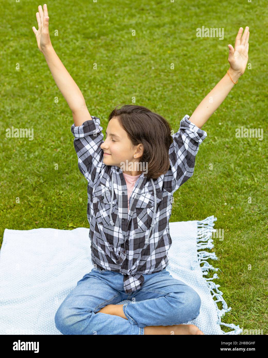 Ritratto giovane bella brunette ragazza sta divertendosi in un parco estivo. Una ragazza carina si siede sull'erba su un copriletto e gode di una calda giornata estiva Foto Stock