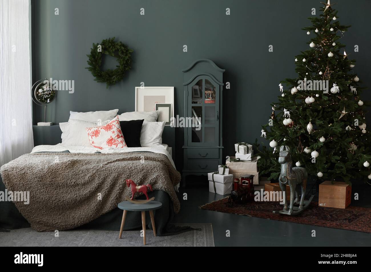 Accogliente camera da letto interno di letto, tappeto, e albero di Natale  con decorazioni natalizie e scatole regalo sullo sfondo della parete grigia  Foto stock - Alamy