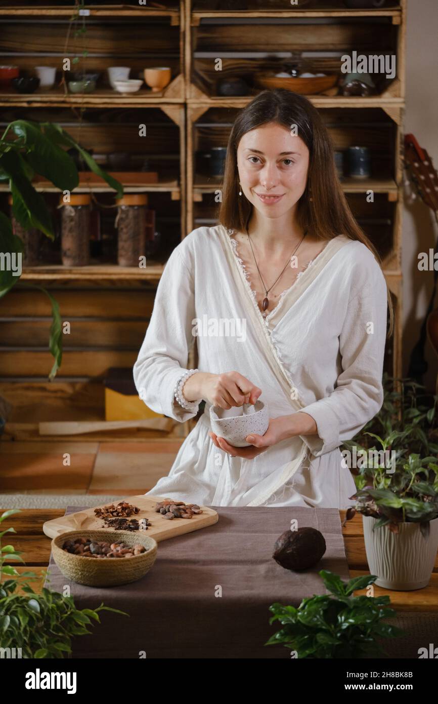 Cerimonia del cacao in uno spazio atmosferico con piante verdi e candele. Donna che fa la bevanda rituale sana dai fagioli di cacao Foto Stock