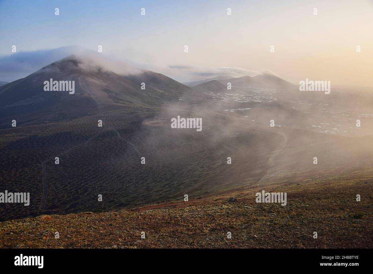 Alba a Lanzarote. Le nuvole di vento di commercio stanno venendo sopra le montagne e si dissolve. Isole Canarie, Spagna. Foto Stock