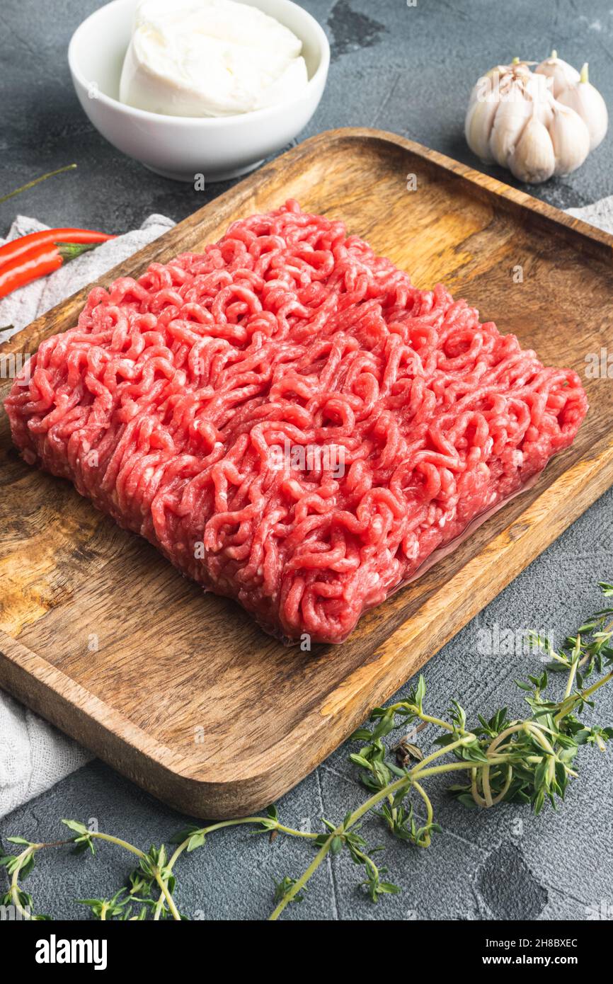 Carne macinata cruda con spezie, verdure ed erbe e polpette di carne, su sfondo di pietra grigia Foto Stock