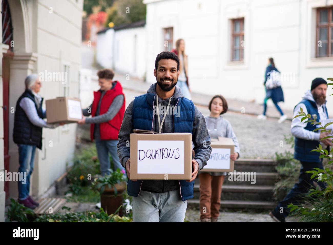 Felice giovane volontario con il team che consegna le scatole di donazione e guardando la macchina fotografica, concetto di assistenza sociale Foto Stock