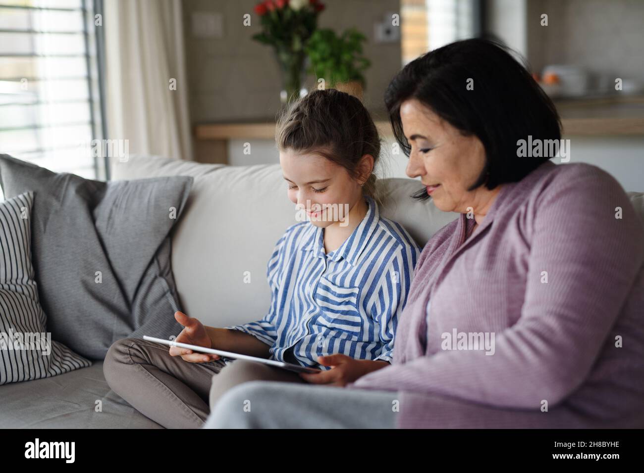 Ragazza piccola felice con nonna in casa, utilizzando tablet. Foto Stock