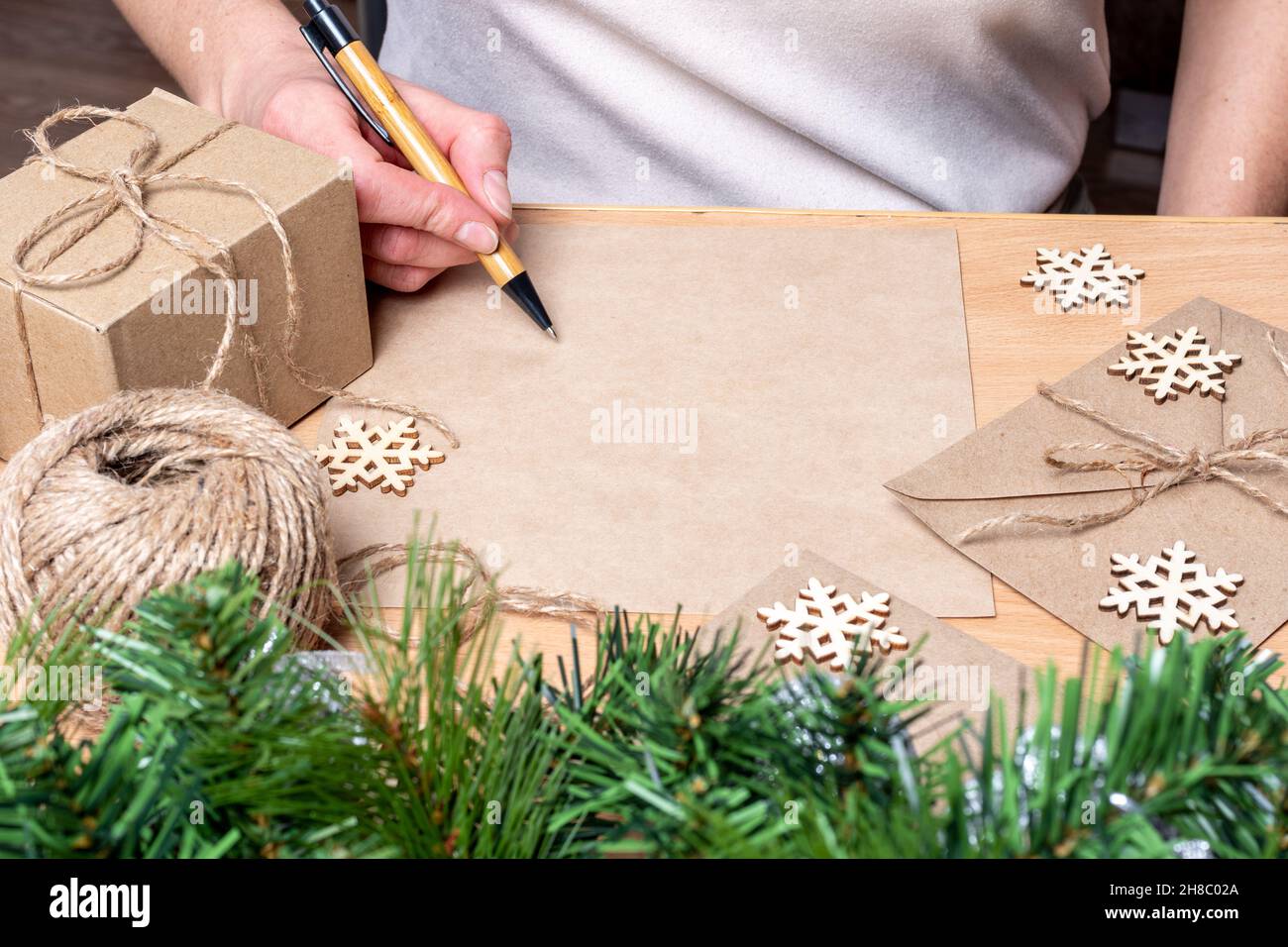 Lista regali - mano che tiene una penna sopra un foglio bianco di carta, regali nelle scatole fatte a mano, fiocchi di neve e rami di abete con le sfere. Concetto per gi ecologico Foto Stock