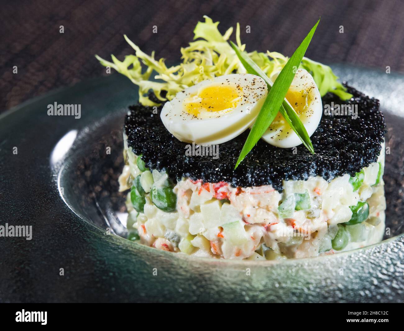 Tradizionale insalata di verdure russe con caviale nero su piastra trasparente su tappetino nero in vimini Foto Stock