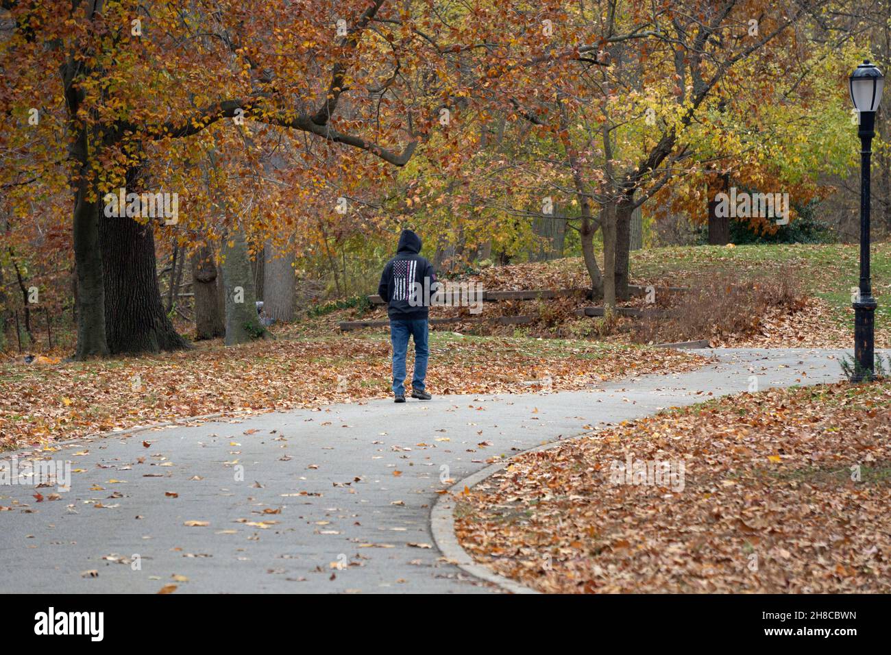 Un uomo anonimo che indossa una felpa con cappuccio e una bandiera americana su una camminata di esercitazione in un pomeriggio coloratissimo di autunno. A Queens, New York Foto Stock