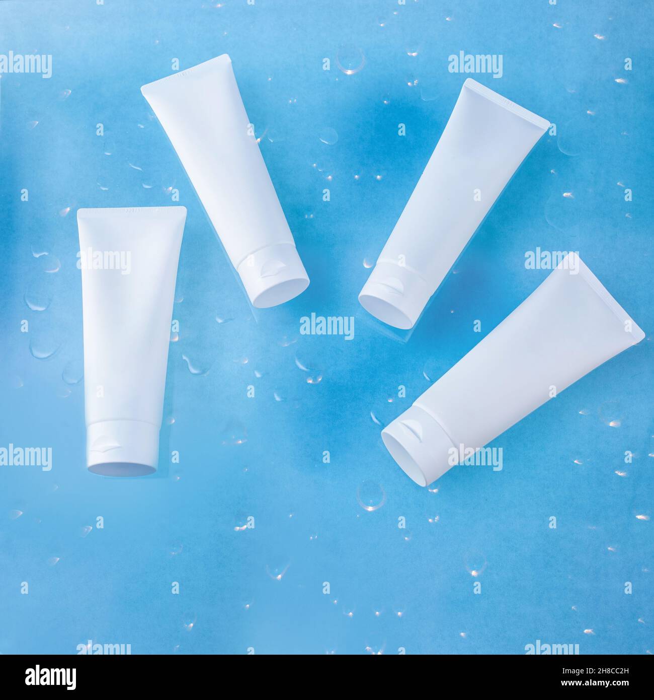 Quattro tubi cosmetici bianchi, con un posto per il testo, giacciono su uno sfondo blu con gocce d'acqua. Foto Stock