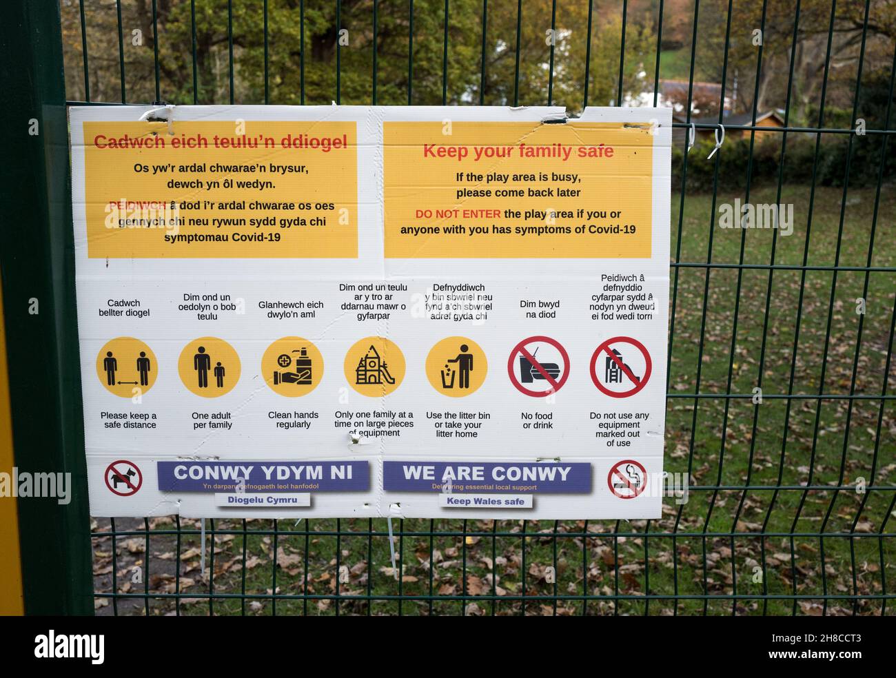 Consigli sanitari e di avvertimento esposti su una recinzione per un'area giochi per bambini in gallese e inglese; Foto Stock