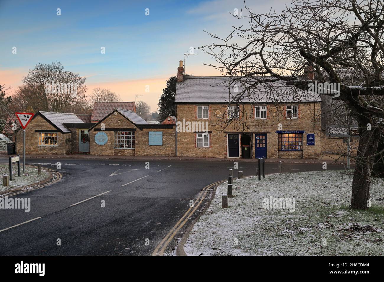 Sharnbrook High Street, Bedfordshire, Inghilterra, Regno Unito - scena invernale all'alba di negozi e cottage sul verde villaggio con gelo e neve sui tetti Foto Stock