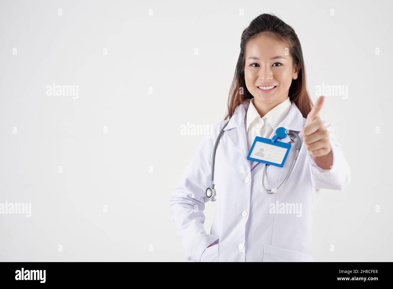 Allegra ragazza piuttosto giovane medico generale sorridente e mostrando i pollici-in su Foto Stock