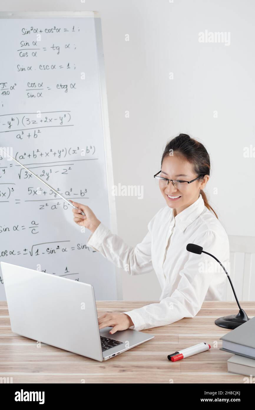Insegnante di college che conduce la lezione in linea, parlando nel microfono e indicando alla lavagna bianca Foto Stock
