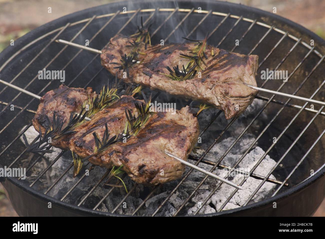 Primo piano di bistecche di gonna marinata con rametti di rosmarino su una griglia per barbecue Foto Stock