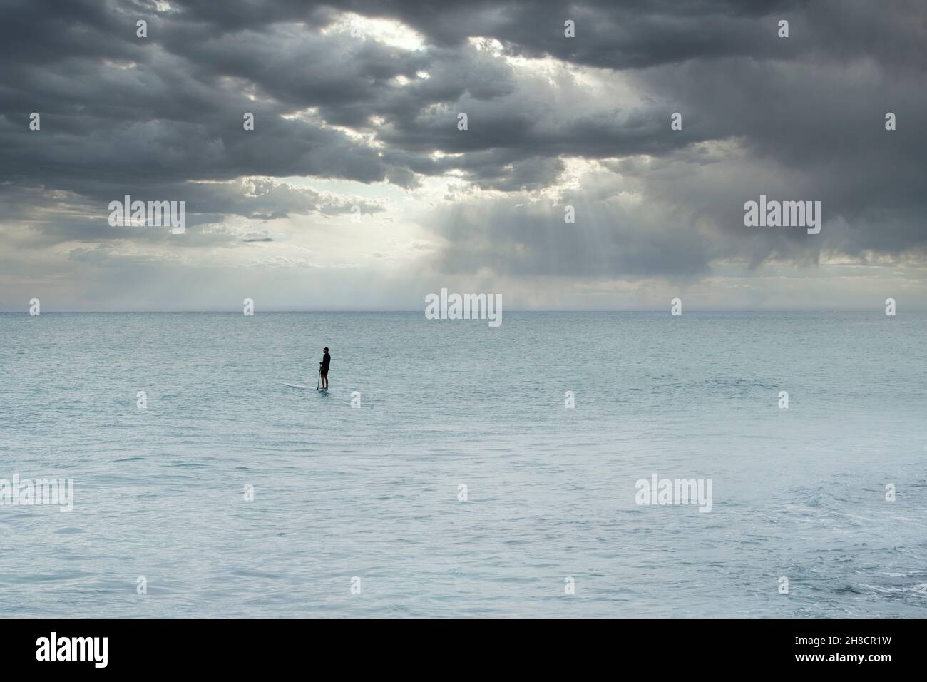 L'uomo solitario nel mezzo del Mar dei Caraibi si paddle su una tavola da paddle contro un cielo tempestoso a Playa del Carmen, Messico Foto Stock