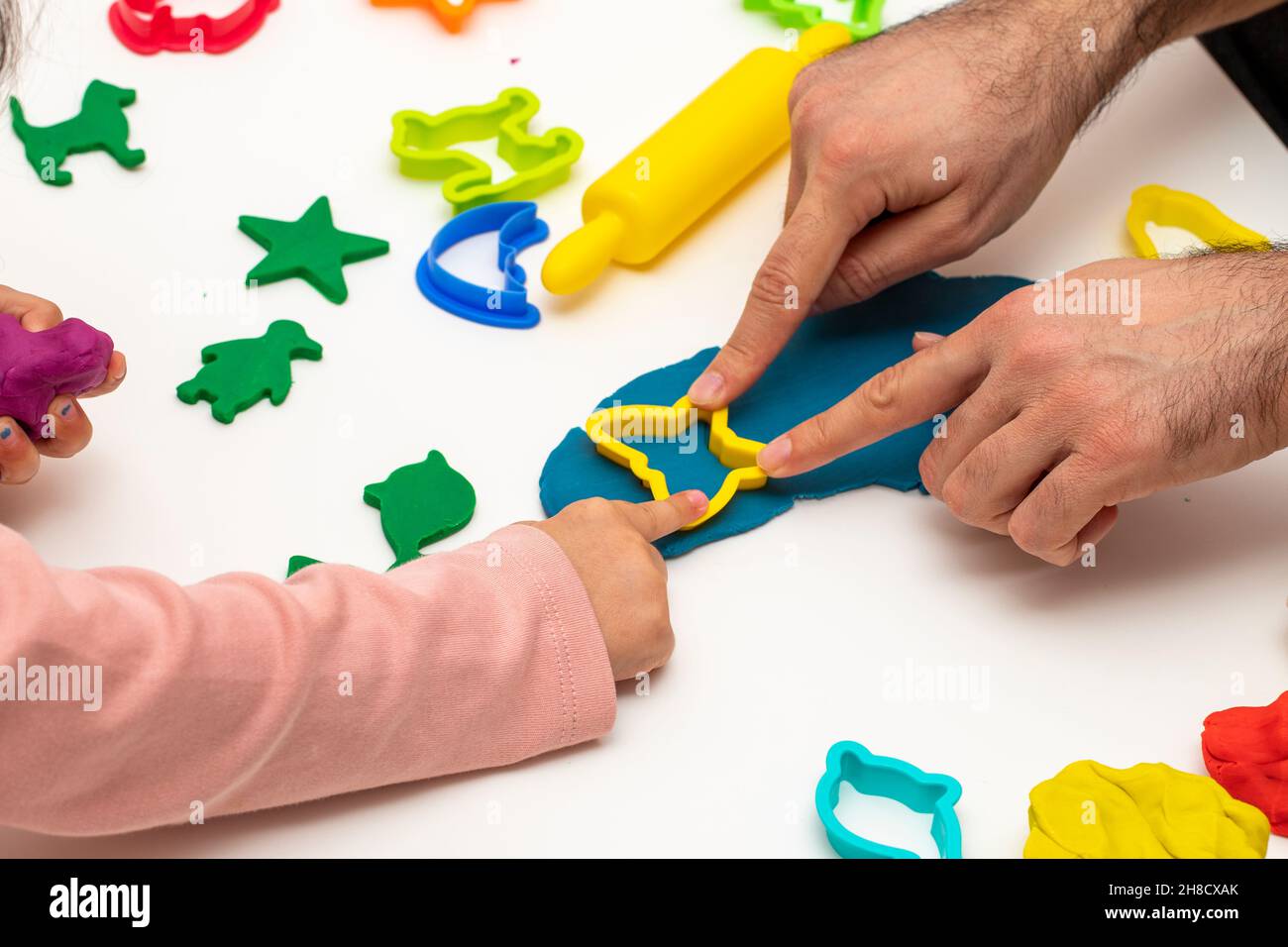 Ragazza che gioca pasta con suo padre. padre figlia che gioca il gioco su sfondo bianco. Realizzazione di varie forme con l'impasto. Primo piano. Festa del Padre Foto Stock