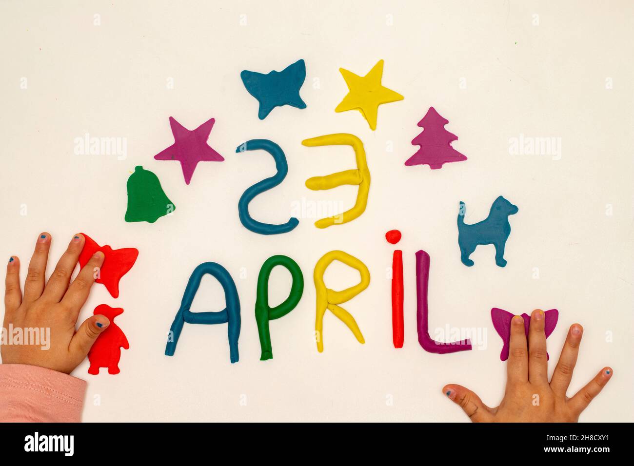 La ragazza scrive il 23 aprile con l'impasto. I bambini giocano con la pasta da gioco su sfondo bianco. Lettera e cifre di aprile 23. 23 aprile giornata mondiale dei bambini Foto Stock
