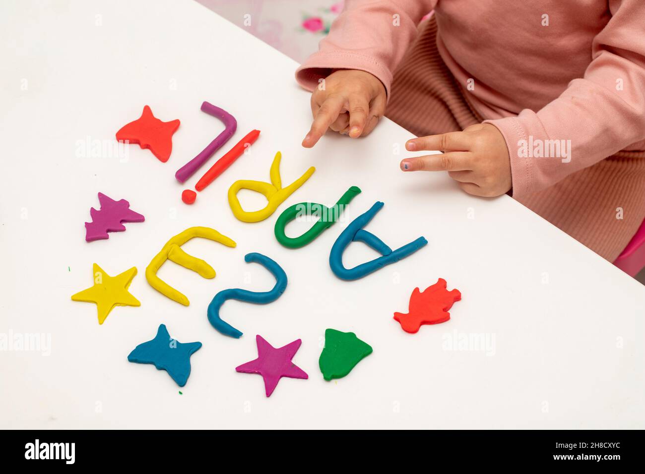 La ragazza scrive il 23 aprile con l'impasto. I bambini giocano con la pasta da gioco su sfondo bianco. Lettera e cifre di aprile 23. 23 aprile giornata mondiale dei bambini Foto Stock