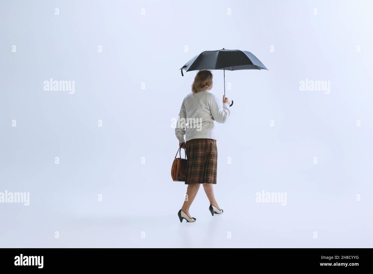Ritratto di donna triste senior in stile retrò, moda degli anni '70, anni '60 a piedi con ombrello isolato su sfondo bianco studio Foto Stock