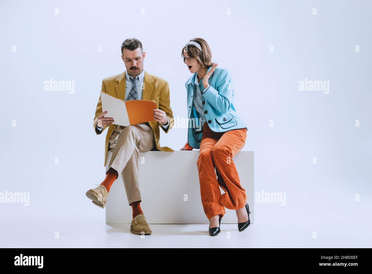 Ritratto di giovane famiglia felice, uomo e donna in stile retrò abiti, moda degli anni '70, sessanta anni seduti insieme isolato su sfondo bianco studio Foto Stock