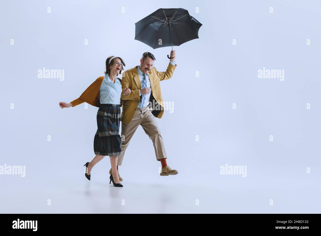 Giovane coppia felice famiglia, uomo e donna in stile retrò abiti, moda degli anni '70, 60 anni a piedi con ombrello isolato su sfondo bianco studio Foto Stock
