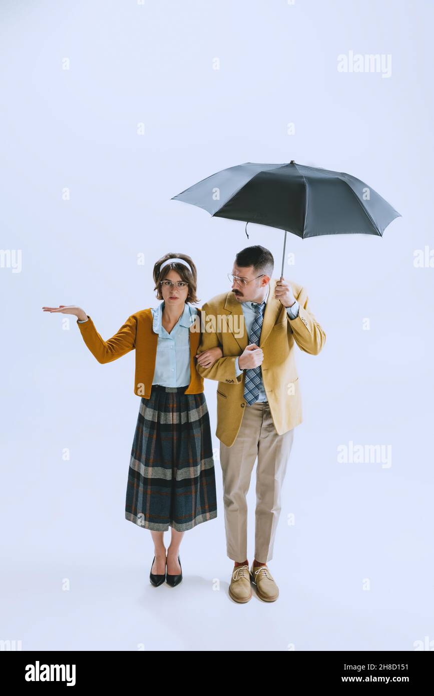 Giovane coppia triste famiglia, uomo e donna in stile retrò abiti, moda degli anni '70, 60 anni a piedi con ombrello isolato su sfondo bianco studio Foto Stock