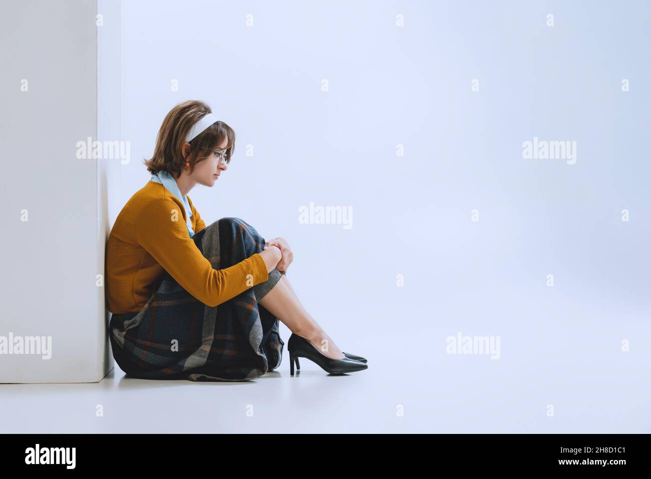 Giovane ragazza triste in stile retrò, moda degli anni '70, anni '80 seduta sul pavimento isolato su sfondo bianco studio con copyspace per l'annuncio. Foto Stock