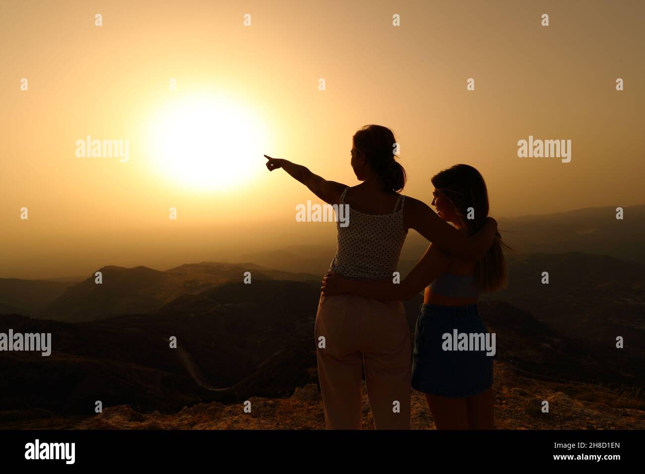 Silhouette con luce posteriore di due donne che puntano il sole al tramonto Foto Stock