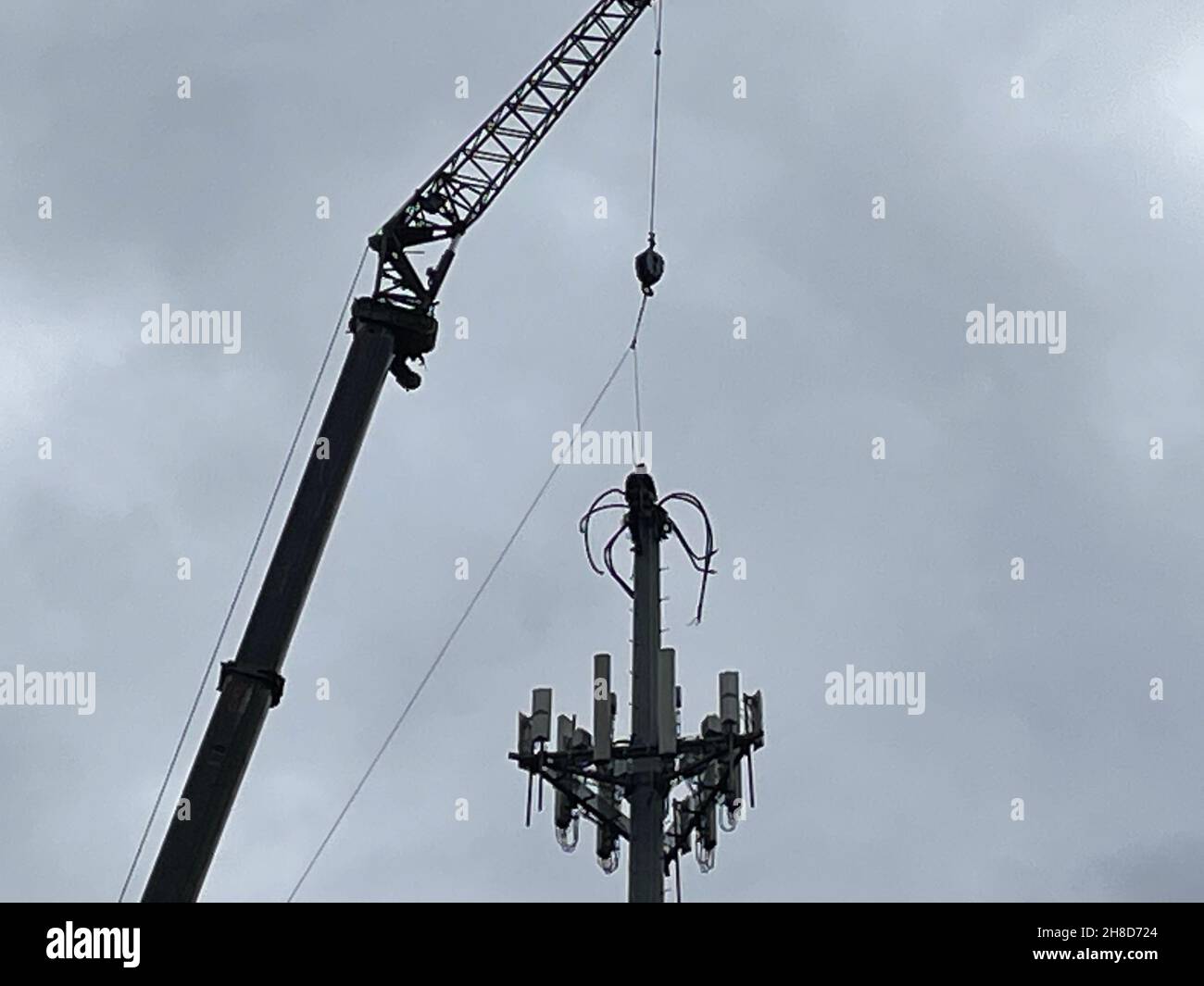 Una persona che lavora in cima a una torre cellulare in alto in una giornata nuvolosa Foto Stock
