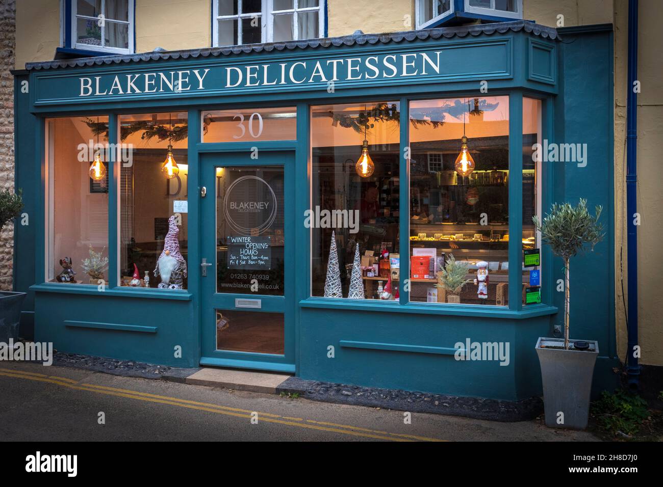 Blakeney Delicatessen su High Street con luci scintillanti in finestra Foto Stock