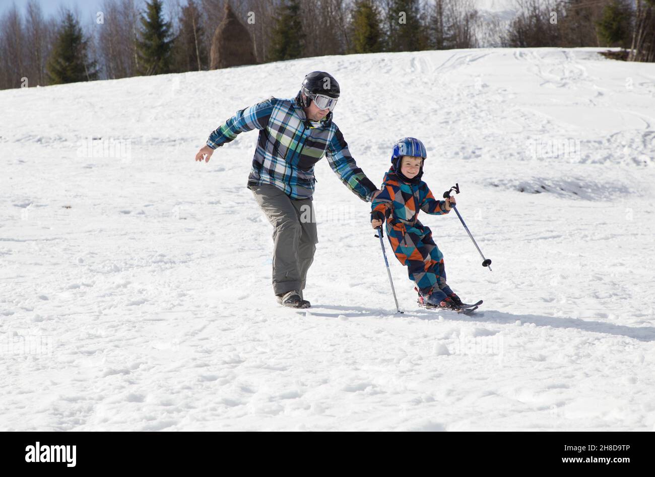 il bambino impara a sciare con il padre nelle montagne innevate in una giornata invernale fredda e soleggiata. Gioie stagionali, buona infanzia, stile di vita sano. Sport e. Foto Stock