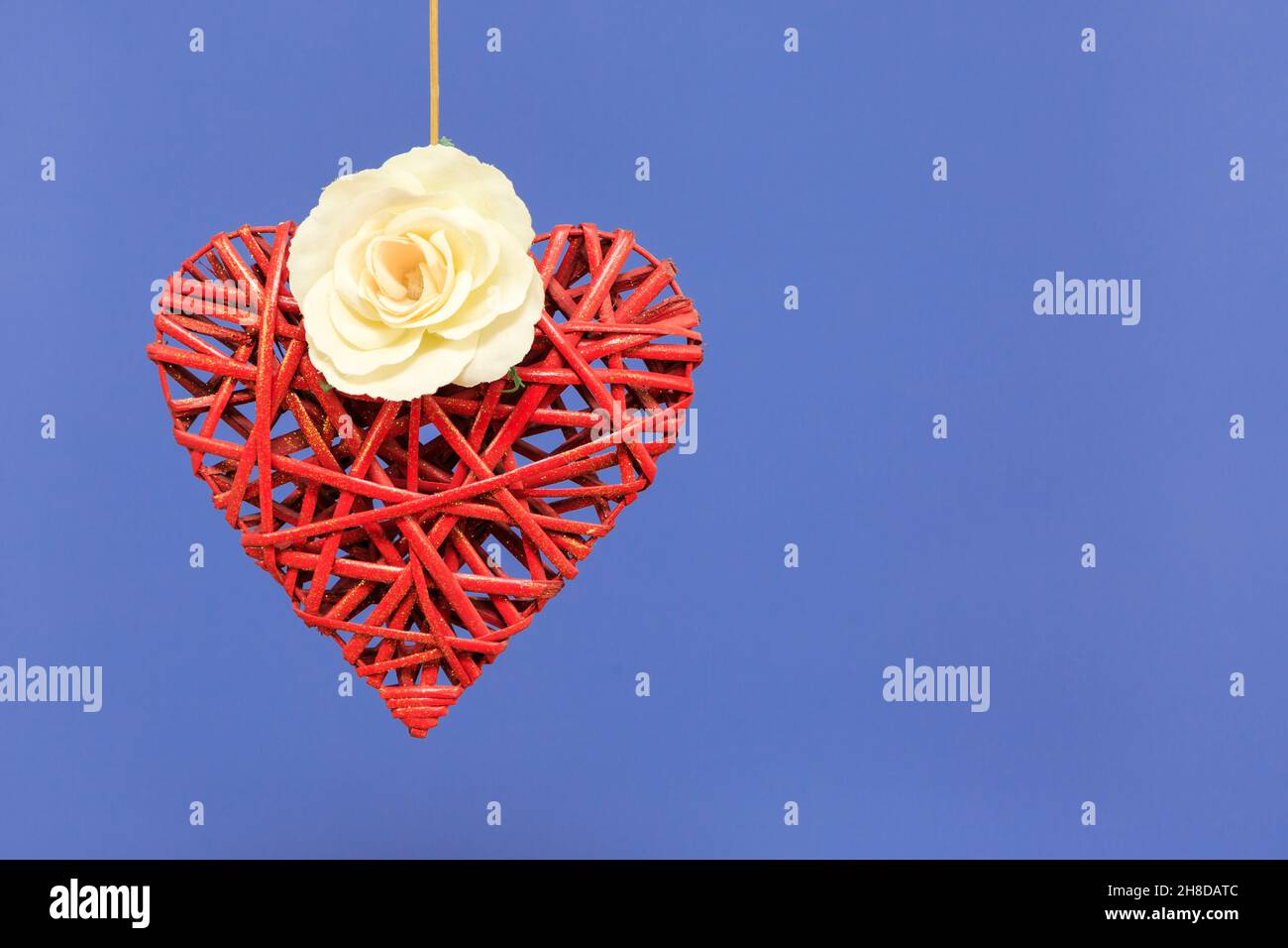 Red Wicker Heart e Single White Rose su sfondo blu Foto Stock