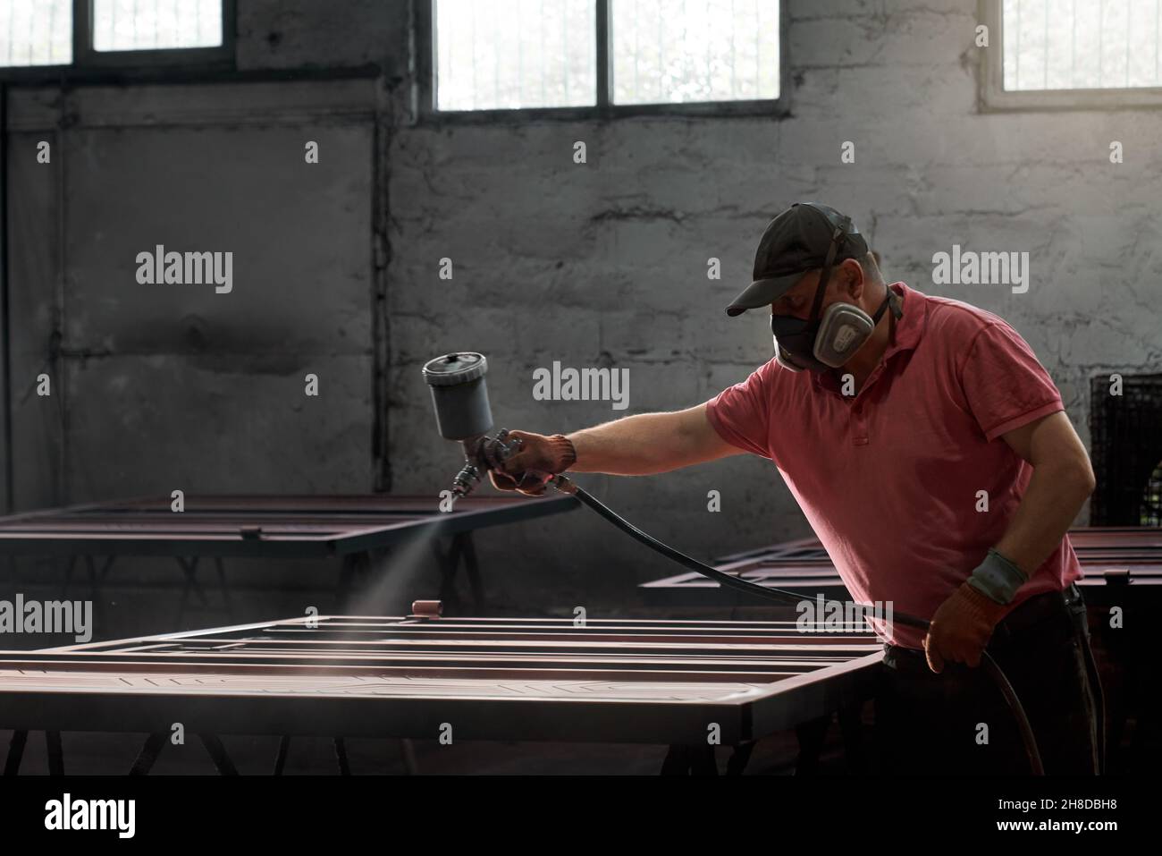 Vista frontale del lavoratore in rosso lavoro maschera di verniciatura uniforme e protettiva cancello con speciale polyviser in officina. Concetto di porta di disegno di processo in luogo speciale. Foto Stock