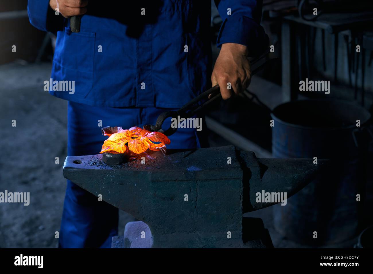 Primo piano di lavoro in uniforme blu scuro in piedi e lavorare con speciali attrezzature di riscaldamento e utensili per la creazione di metallo in smithy. Concetto di processo che fa recinto moderno. Foto Stock