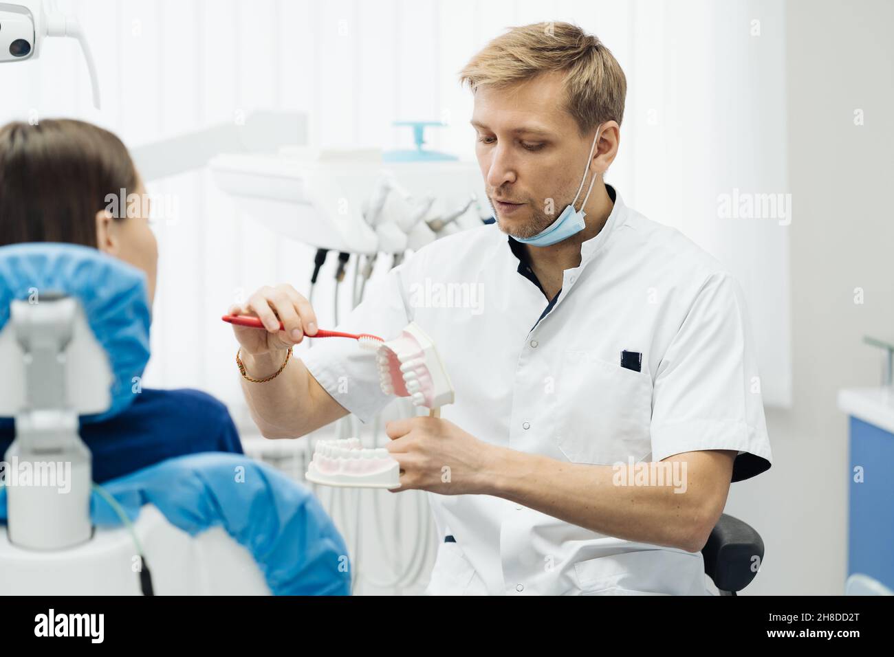 Dentista che mostra la corretta igiene dentale utilizzando mock-up di scheletro di denti. Medico stomatologo che spiega la corretta igiene dentale per il paziente che tiene un campione di mandibola umana con spazzolino da denti. Foto Stock