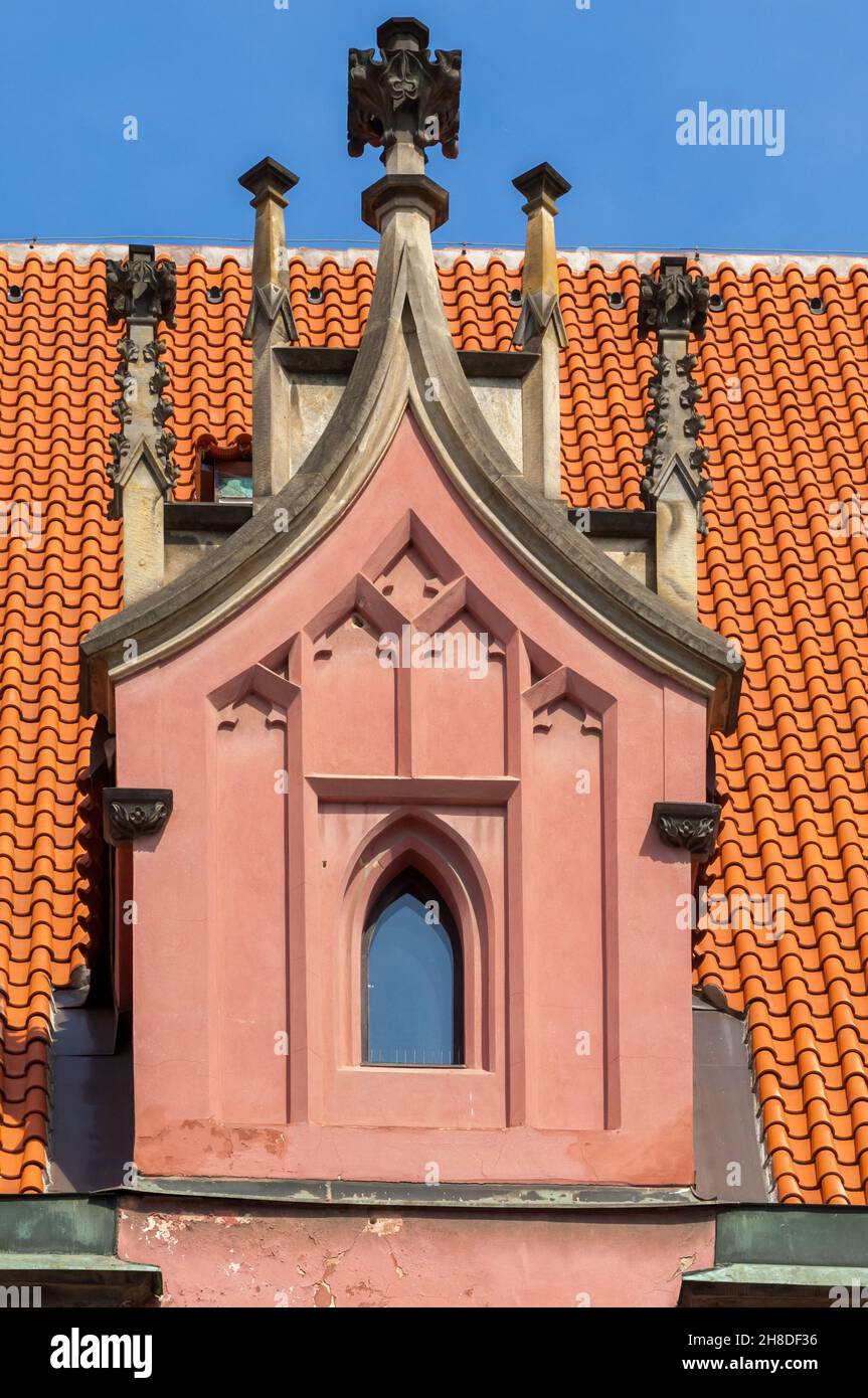 Una finestra dormitorio ornata sporge dal luminoso tetto in terracotta arancione della West House, una storica casa mercantile nella Staroměstské nám di Praga Foto Stock