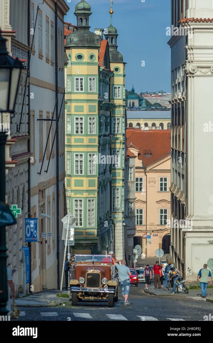 Le cupole a cipolla verde si affacciano sul colorato Palace Smiřických di Malostranské náměstí, mentre un'auto turistica di Praga d'epoca ti aspetta personalizzata in strada Foto Stock