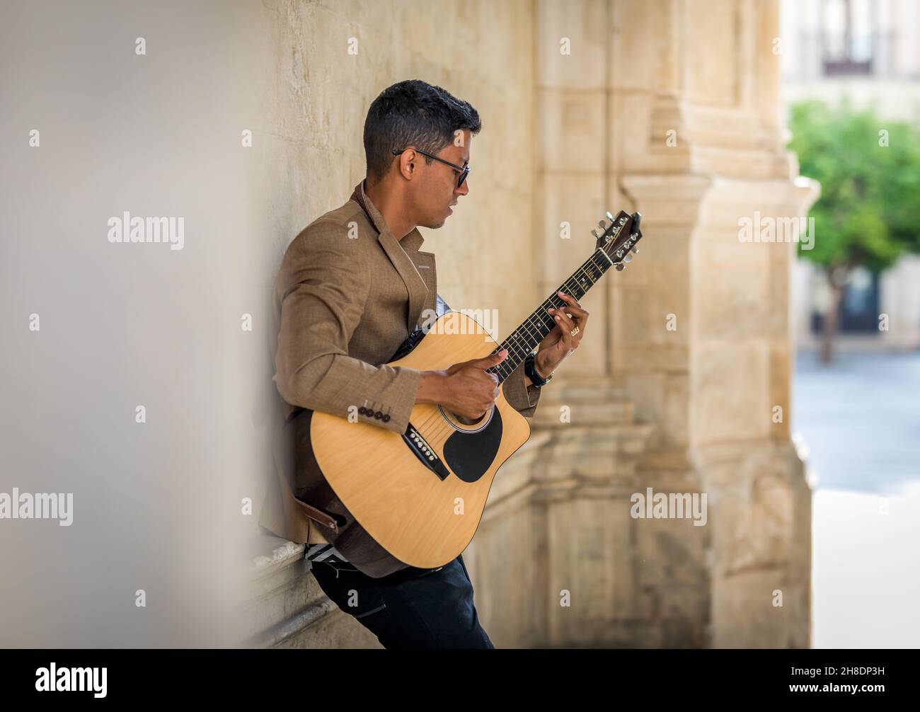 Uomo latino con gli occhiali che suonano la chitarra per strada Foto Stock