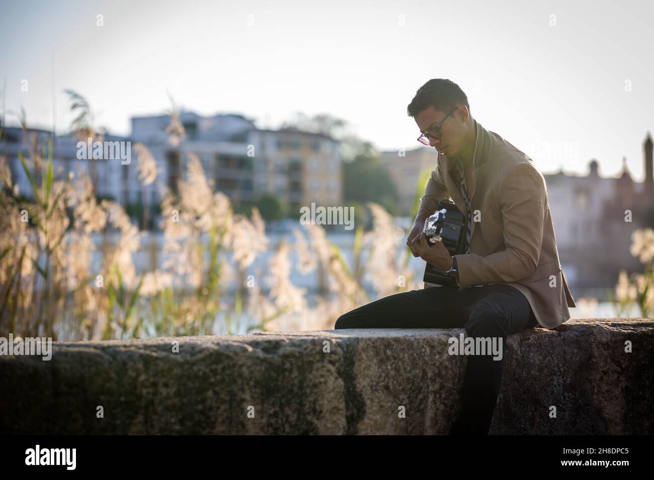 L'uomo latino suona la chitarra per strada durante il tramonto contro la luce Foto Stock